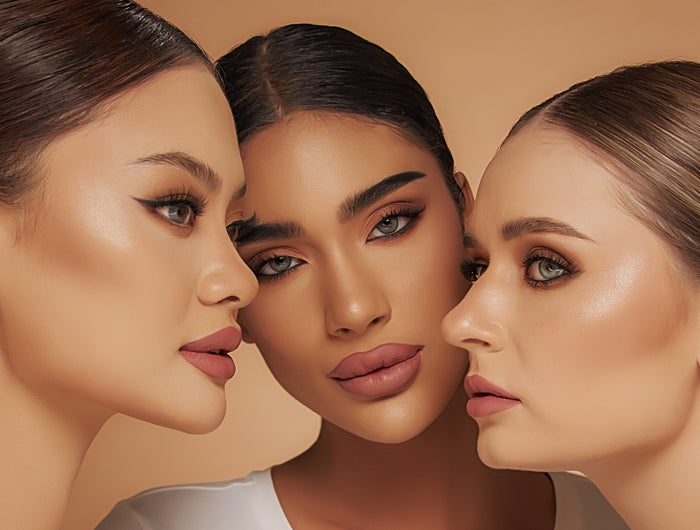 Three women in white shirts posing closely together against a beige background